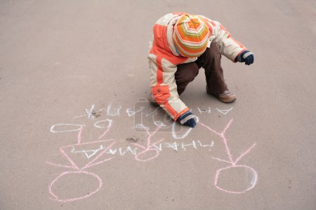 Boy sketches by chalk on asphalt