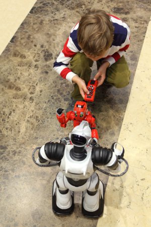 Little boy playing with two radio controlled robots view from ab