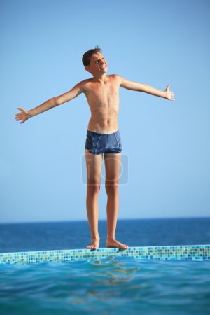 Teenager boy standing near pool against sea, Plants hands in par