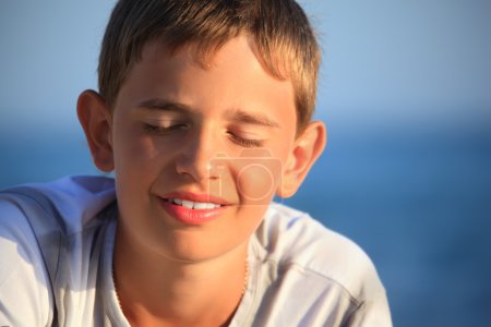 Smiling teenager boy against sea, closed eyes