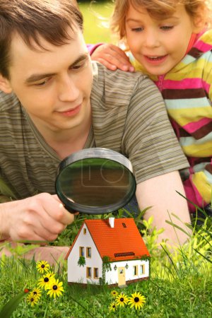 Father with little girl looking on small house through magnifier