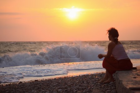 Silhouette sitting young woman on sunset wavy beach
