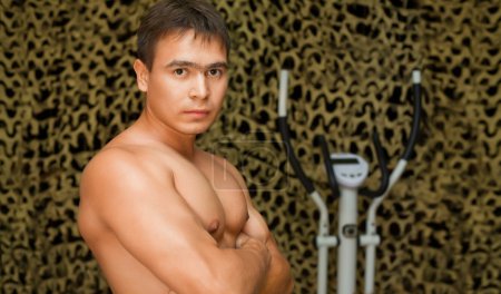 Strong bodybuilder training muscles in gym, posing at camera