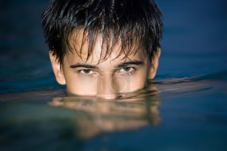Teenager boy swimming in pool at night, having plunged on eyes i