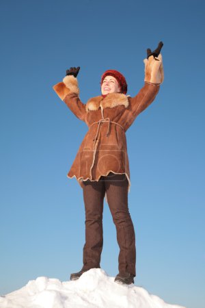 Pretty young woman stand on snow hill with hands up