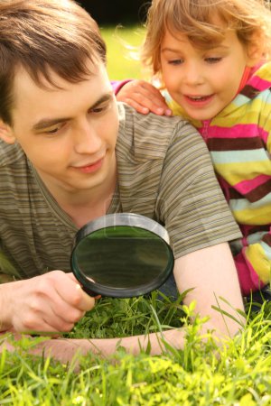 Young man and little girl look through magnifier