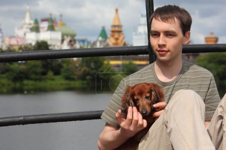 Young man holds dachshund on hands outdoor in summer