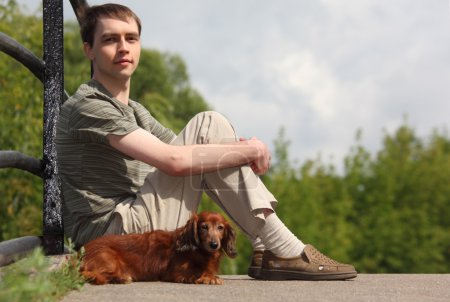 Young man and his dachshund sits outdoor in summer