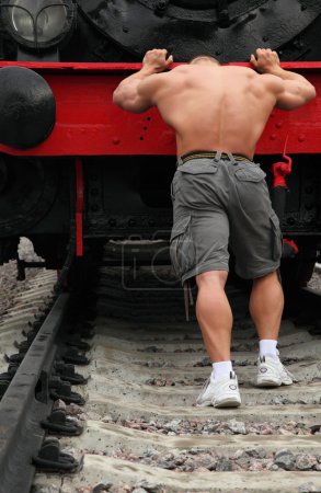 Strong shirtless man pushs locomotive