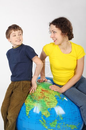 Mother and son sitting on big inflatable globe, smiling and look