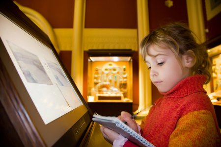 Little girl standing near monitor writes to writing-books at exc