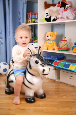Little boy in playroom on toy zebra