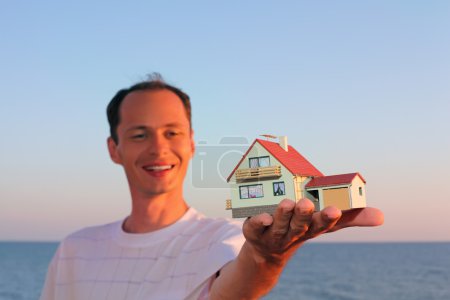 Young man keeps in hand model of house with garage