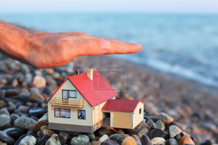Model of house with garage on stony beach in evening, Man's hand