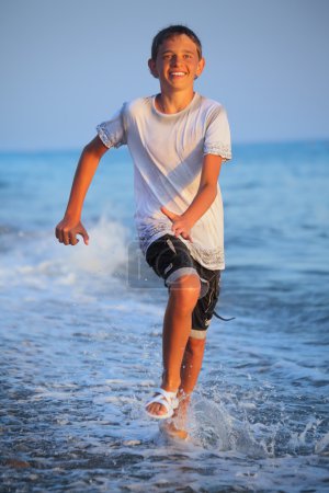 Teenager boy running in wet clothes on beach