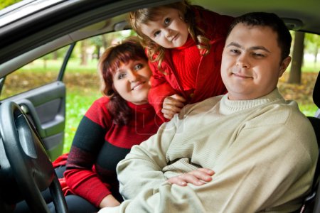 Married couple and little girl sit in car in park