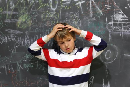 Pupil standing near school board and hold on his head half body