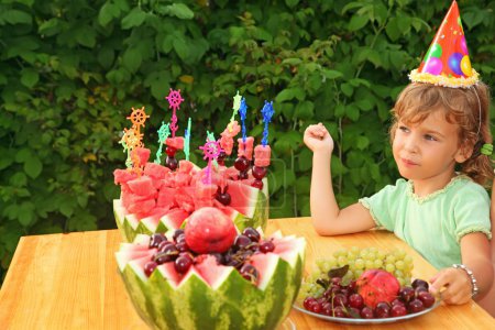 Little girl eats fruit in garden, happy birthday party seven yea