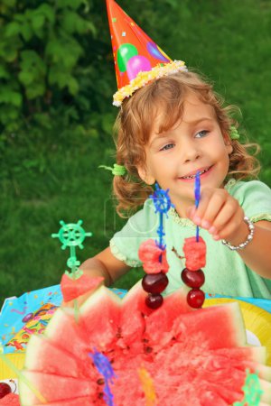 Little girl in cap eats fruit in garden,happy birthday