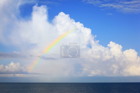 White big clouds and multi-coloured rainbow over sea in afterno