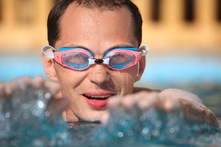 Young man in watersport goggles swimming in pool, extended hands