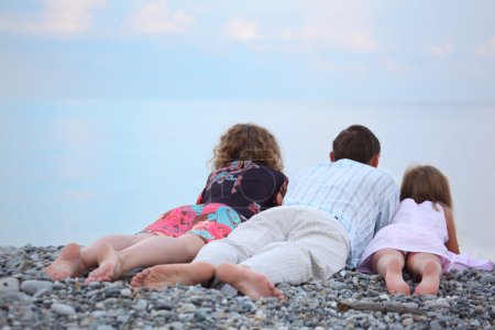 Happy family with little girl lying on stony beach, lying back