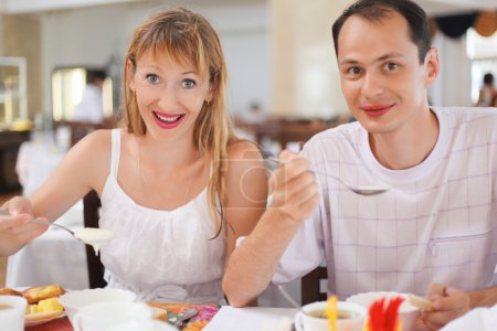 Married couple having breakfast at restaurant, eating cream whea