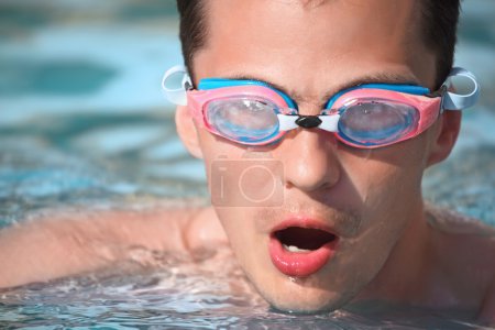 Young man in watersport goggles swimming in pool, taking breath