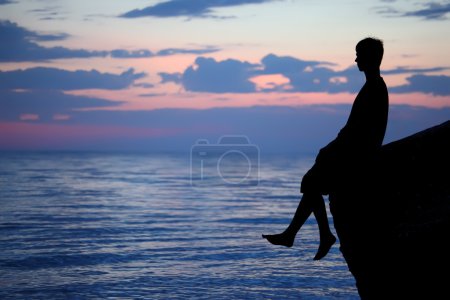 Silhouette guy sitting on breakwater in evening near sea