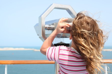 Little girl standing on cruise liner deck and looking in binocul