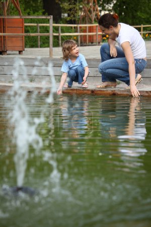 Mother with daughter in park at pool with fountain touch water