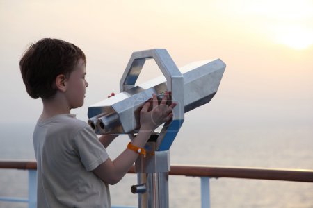 Little boy standing near binocular and looking into the distance