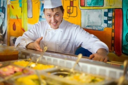 Cheerful cook in uniform near counter with meal