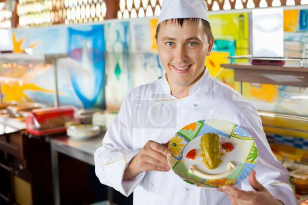 Cheerful cook in uniform holding in hands dish with salad in for