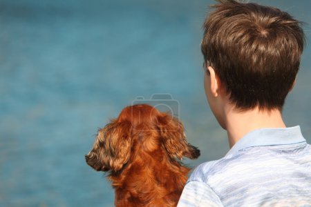 Young man and his dachshund from back outdoor against water