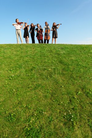 Group of musicians play violins on hill against sky