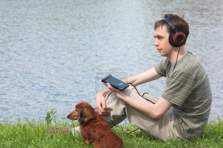 Young man liistens music in headphones sits on grass with his da