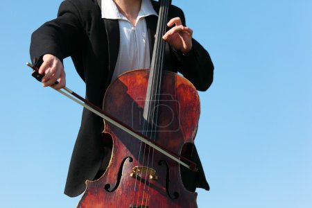 Close-up musician plays violoncello against sky