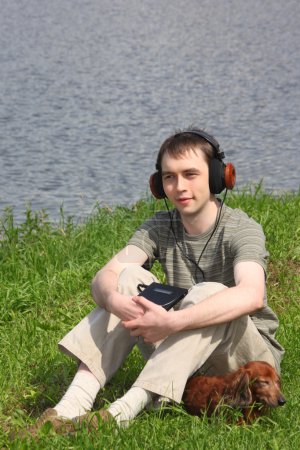 Young man liistens music in headphones sits on grass with his da