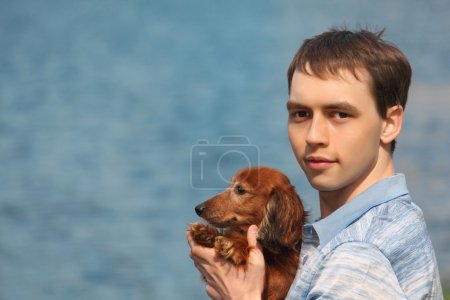 Young man and his adorable dachshund closeup against water