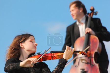 Violinist and violoncellist play against sky