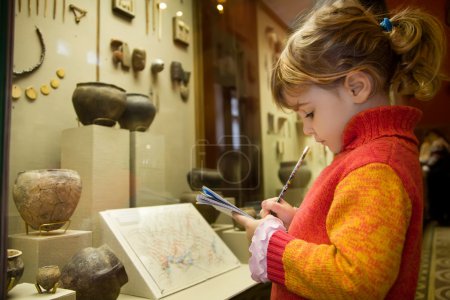 Little girl writes to writing-books at excursion in historical m