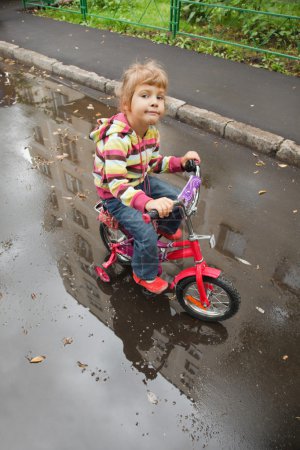 Girl goes on a bicycle on wet asphalt