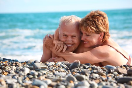 Happy aged pair lie on pebble beach