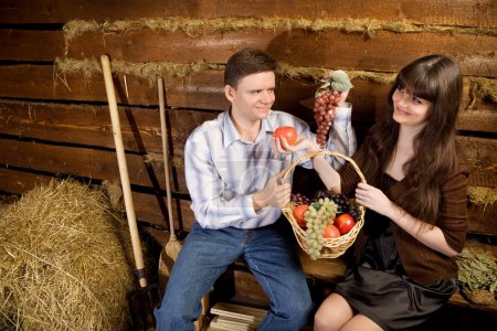 Smiling man and woman with basket of fruit sitting on bench