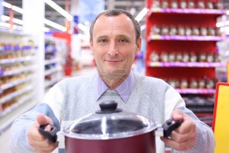 Elderly man in shop with pan in hands