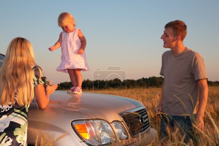 Parents and child on car cowl on wheaten field