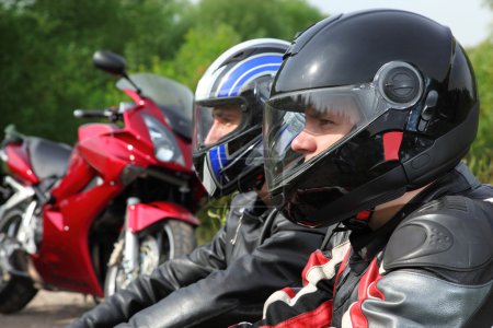 Closeup of two motorcyclists sitting on country road near bikes