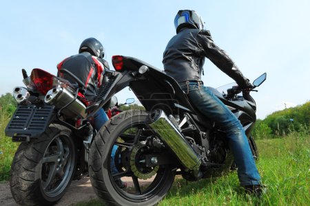 Two motorcyclists standing on country road, back view