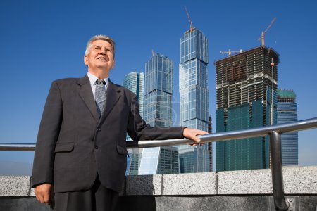 Smiling senior man in suit near skyscrapers construction